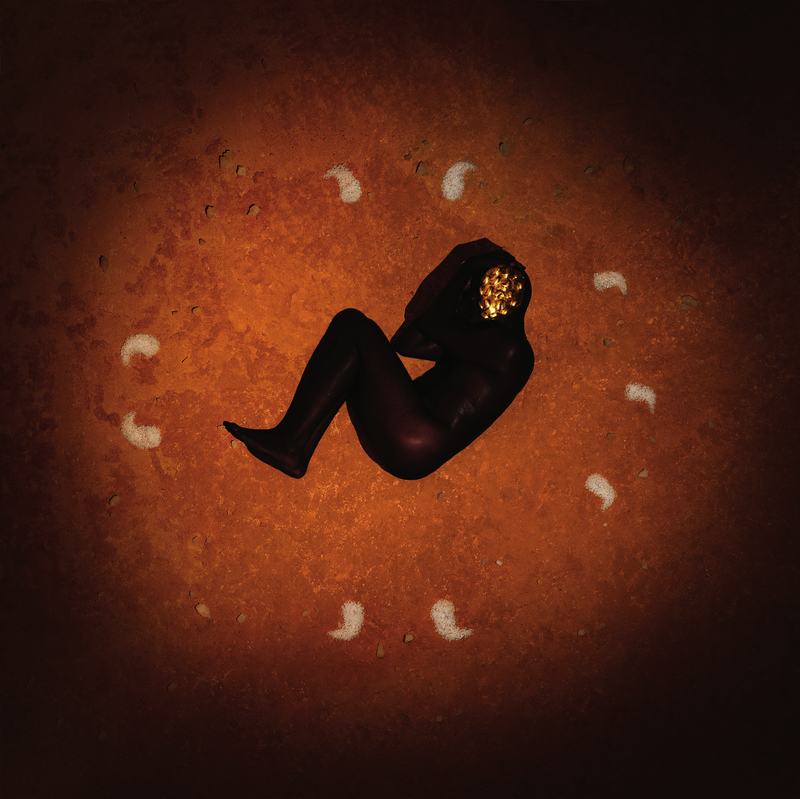 A figure lies coiled on red earth inside a ring of salt, a brass mask over the face.