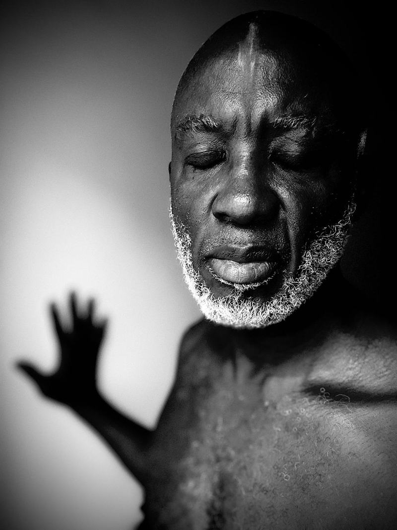Olubode, eyes closed, one hand raised, in black and white.